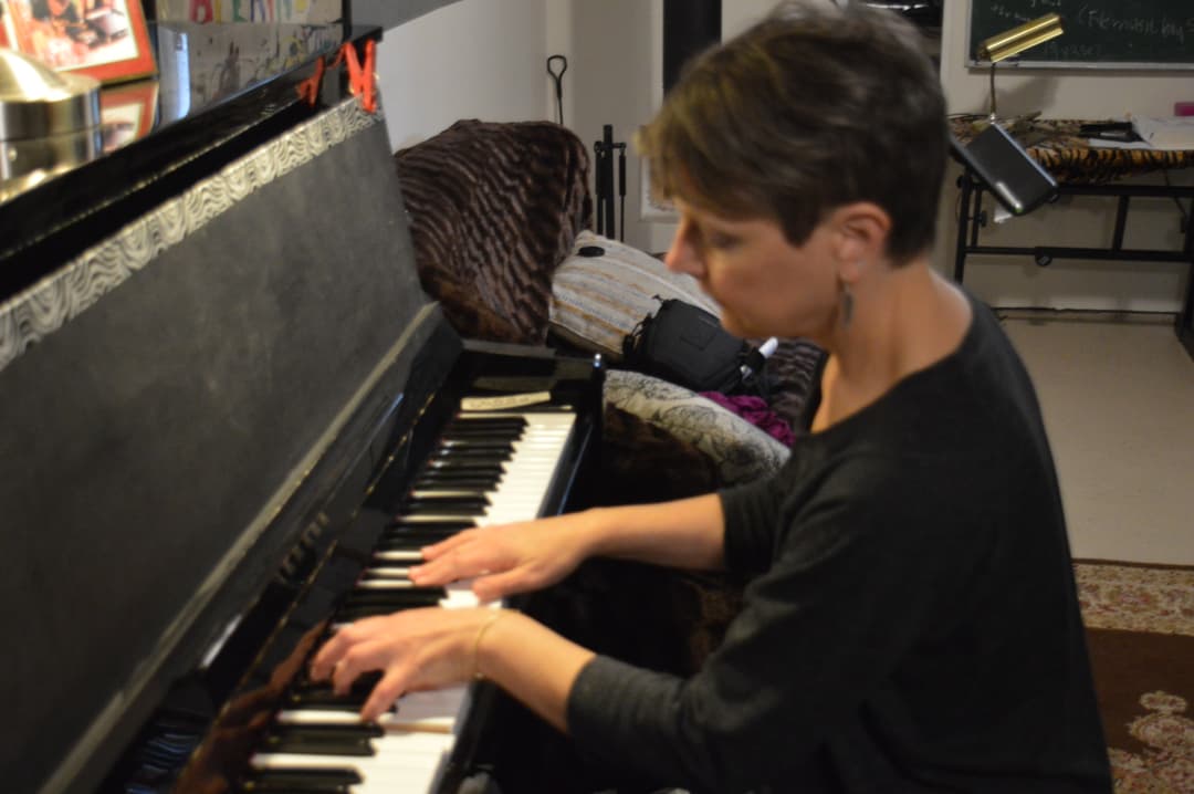 Photo of Lisa St. Clair playing an upright piano in a home studio